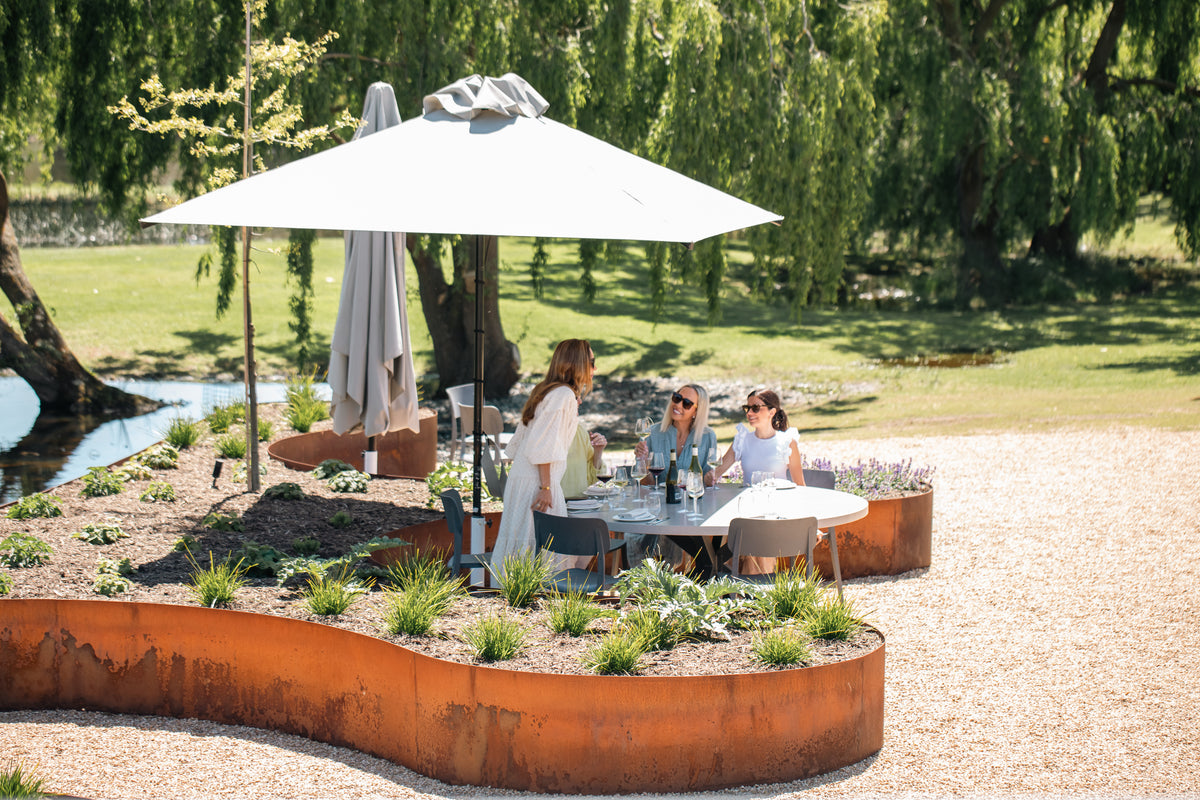 Guests lunching under an umbrella on the Terrace, beside a garden bed