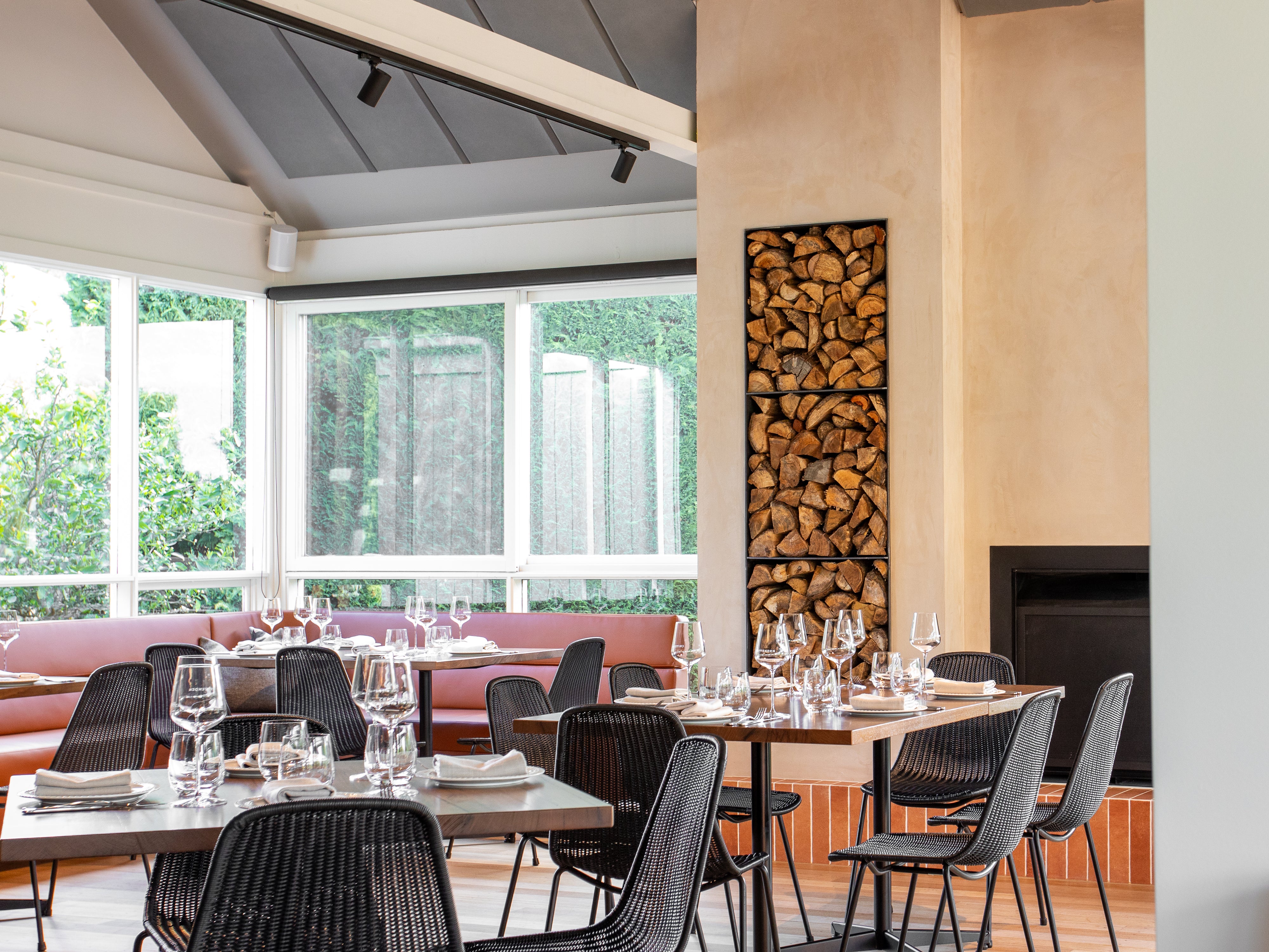 The restaurant dining room with set tables, a wood stack and garden windows