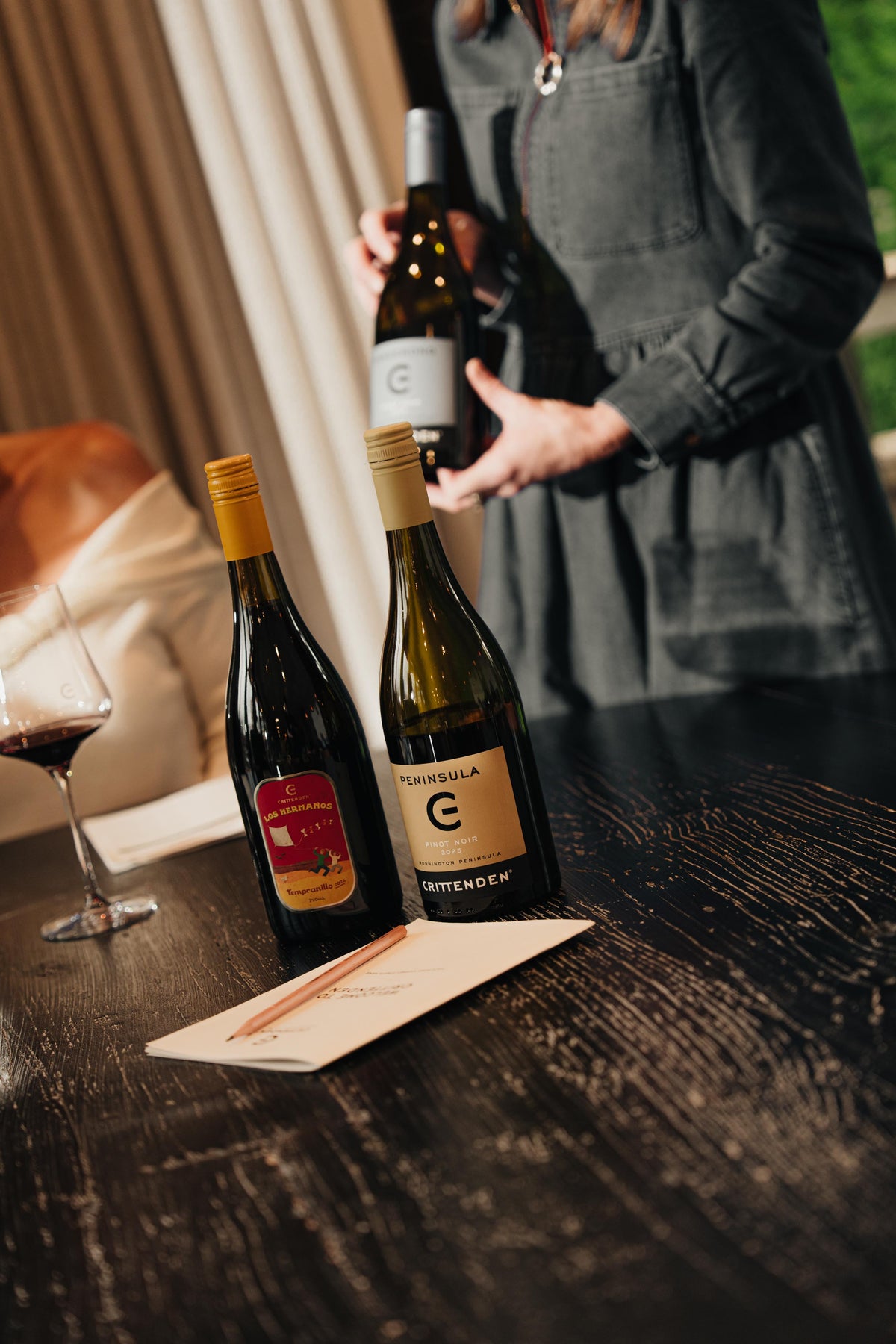 A host presenting a bottle of Crittenden white beside two other wines at a tasting