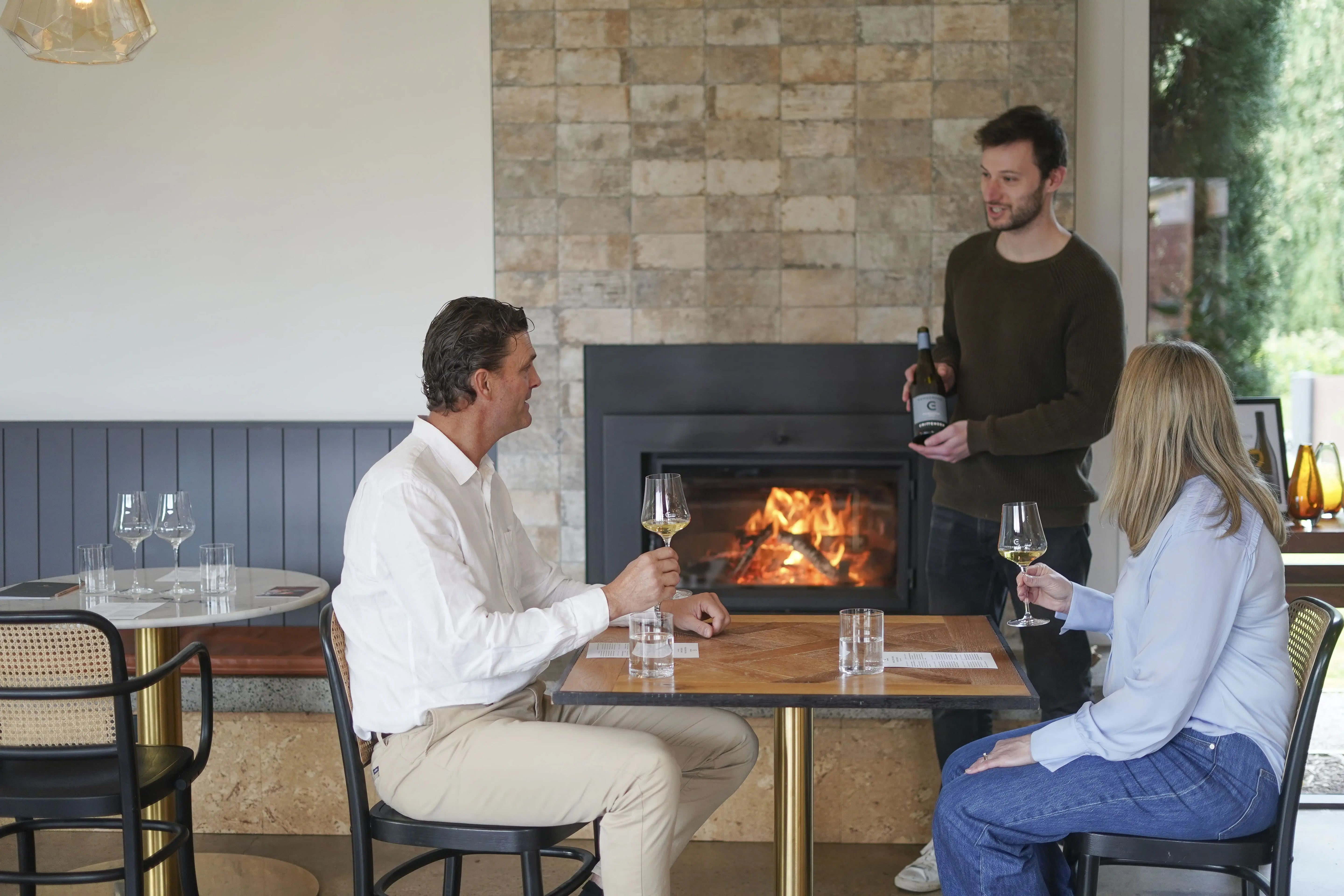 Two men and a woman sitting at a table in a cozy room with a fireplace enjoying a wine tasting at Crittenden