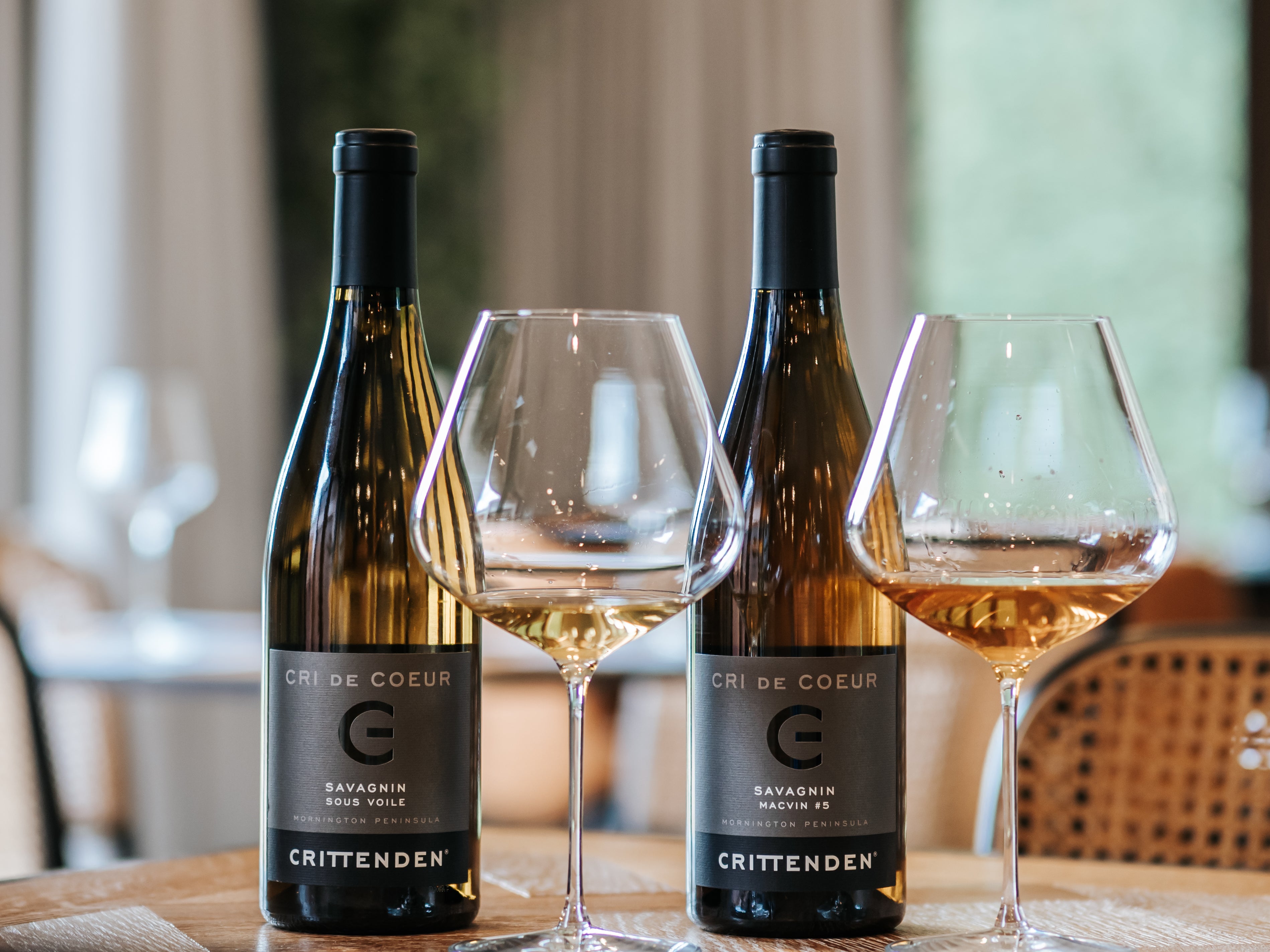 Two bottles of Cri de Coeur Savagnin and Macvin with glasses on a restaurant table