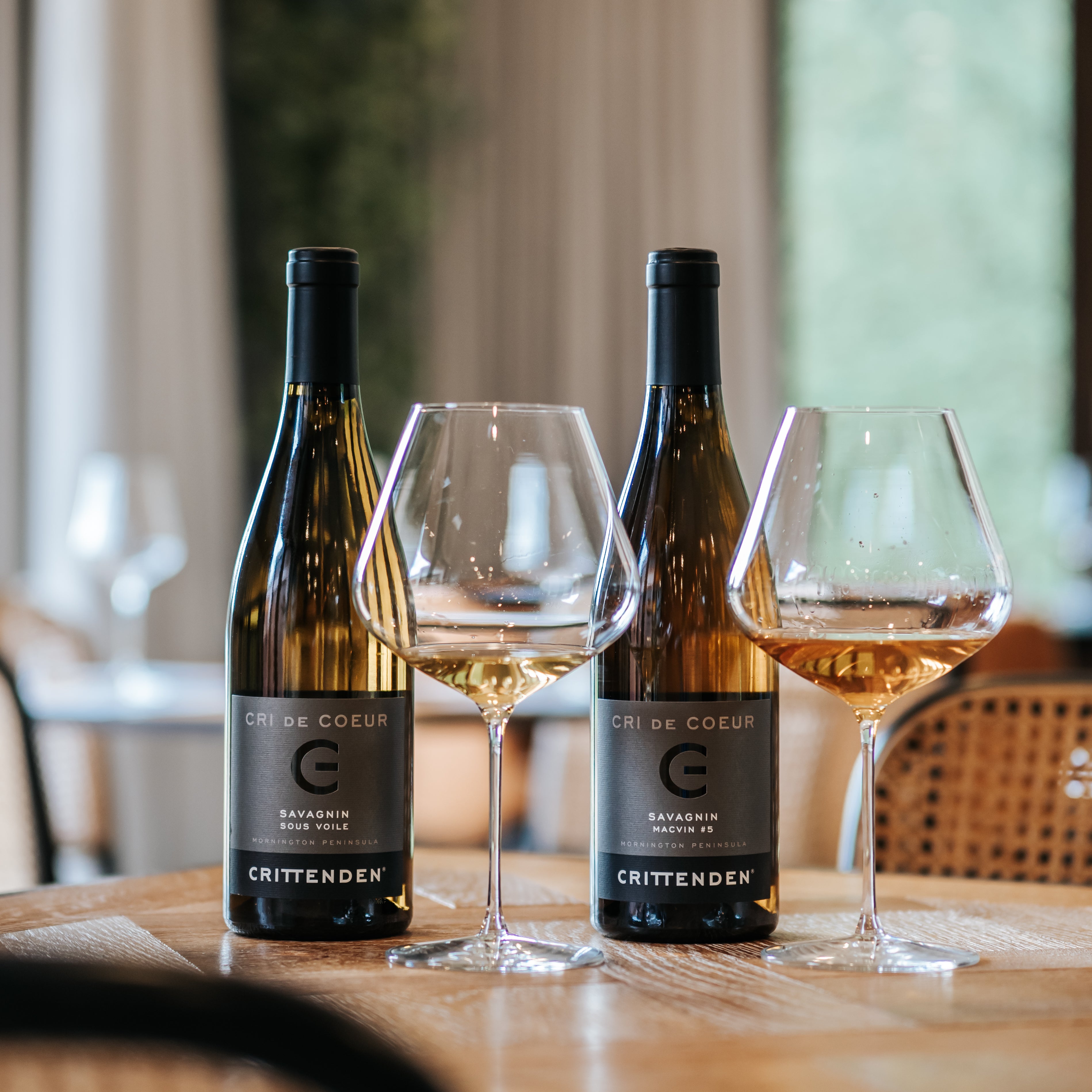 Two bottles of Cri de Coeur Savagnin and Macvin with glasses on a restaurant table
