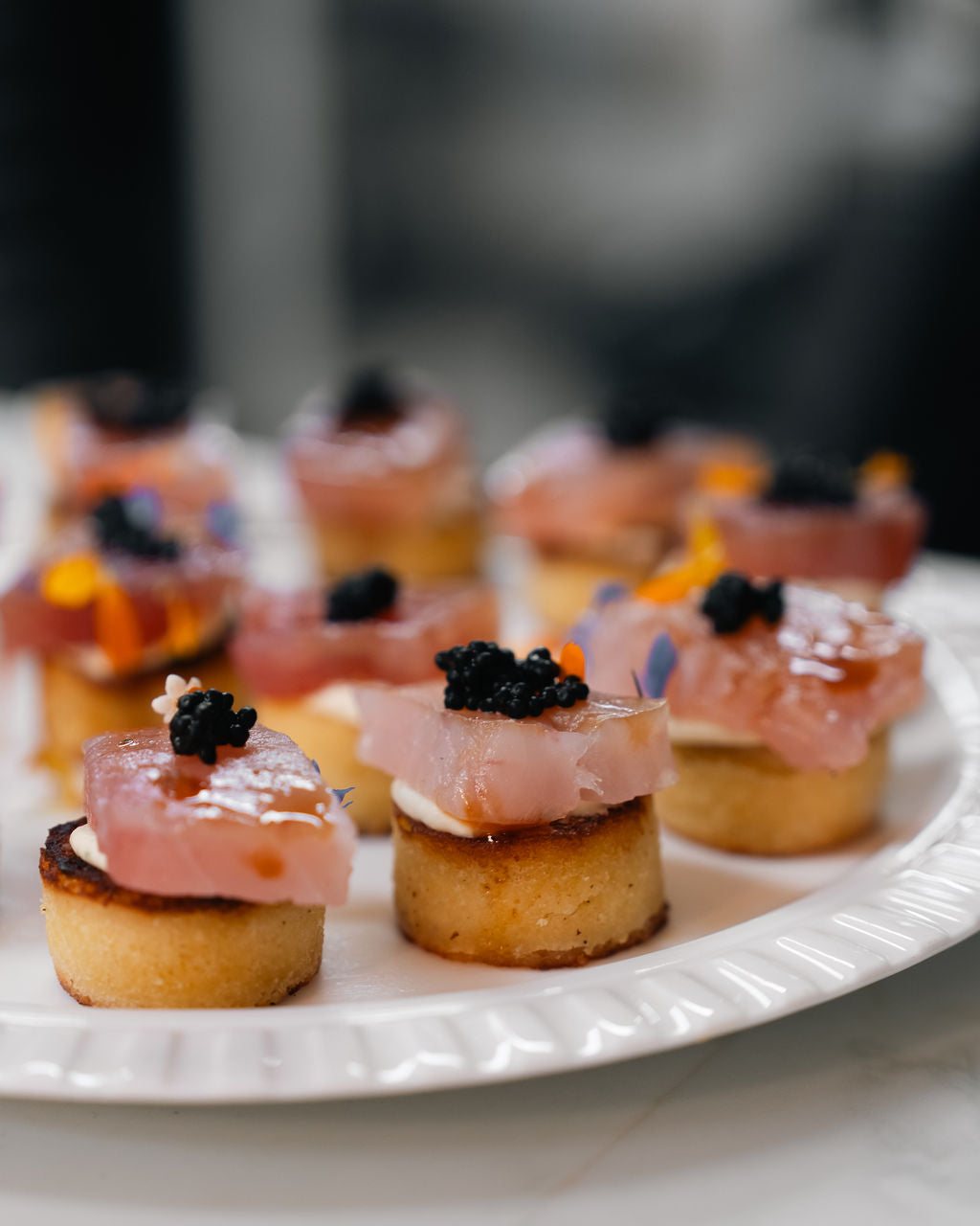 Canapés topped with fish and caviar on a white platter