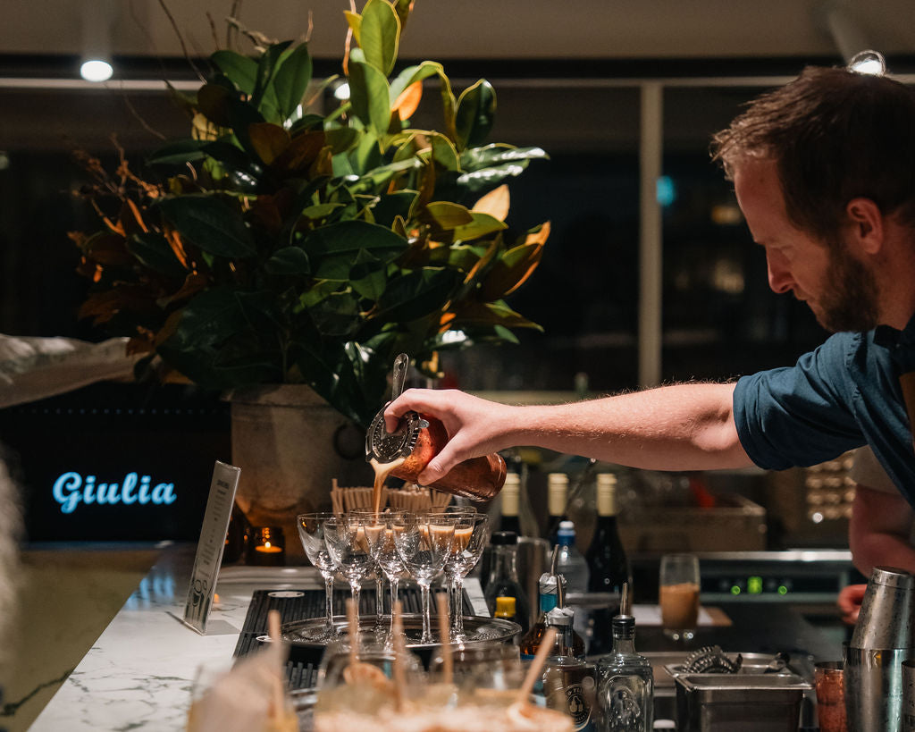 A bartender pouring a drink into a tower of glasses