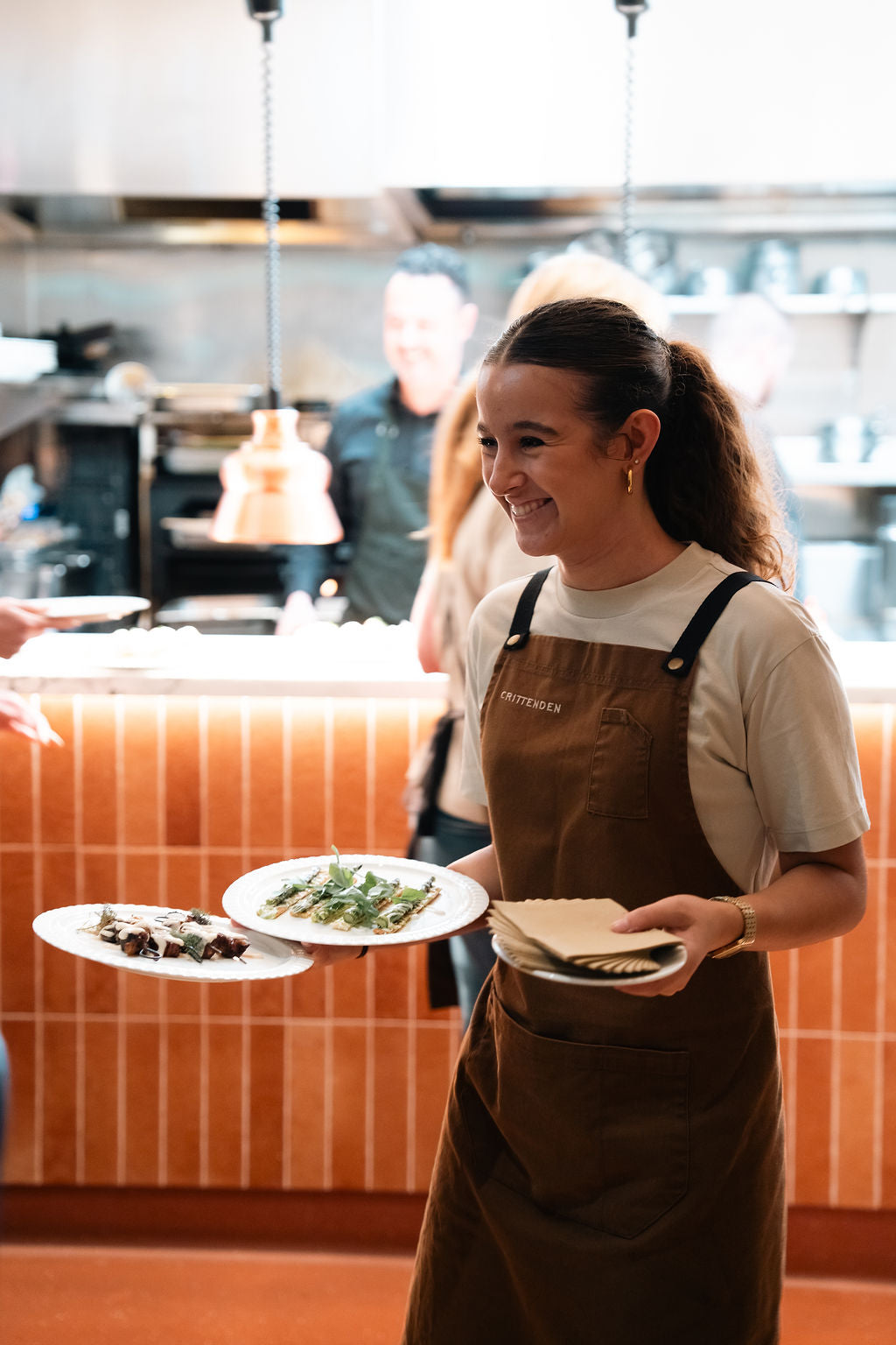 A server smiling as she carries two plates from the open kitchen
