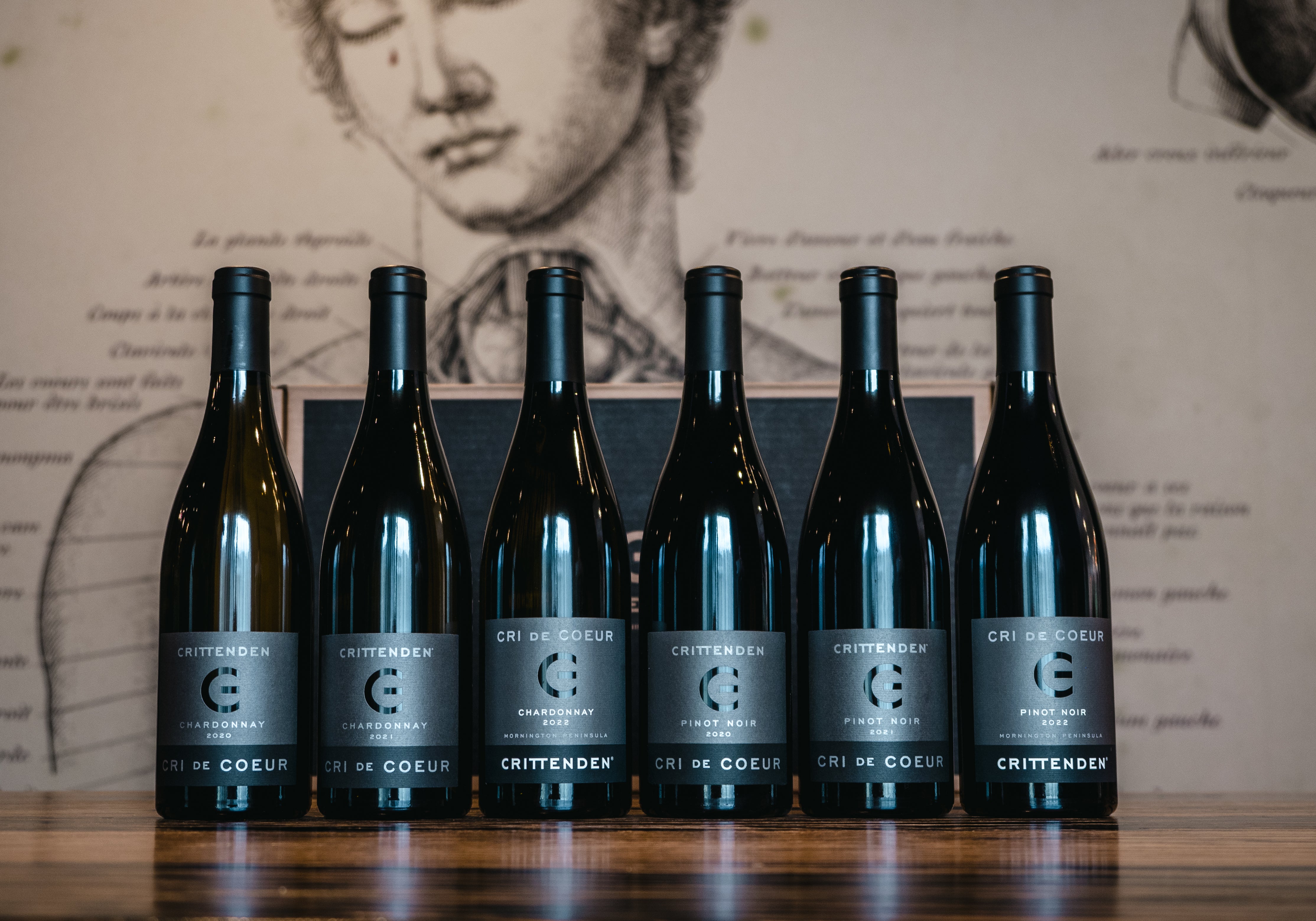 Six bottles of Cri de Coeur Chardonnay and Pinot Noir lined up on a timber bar
