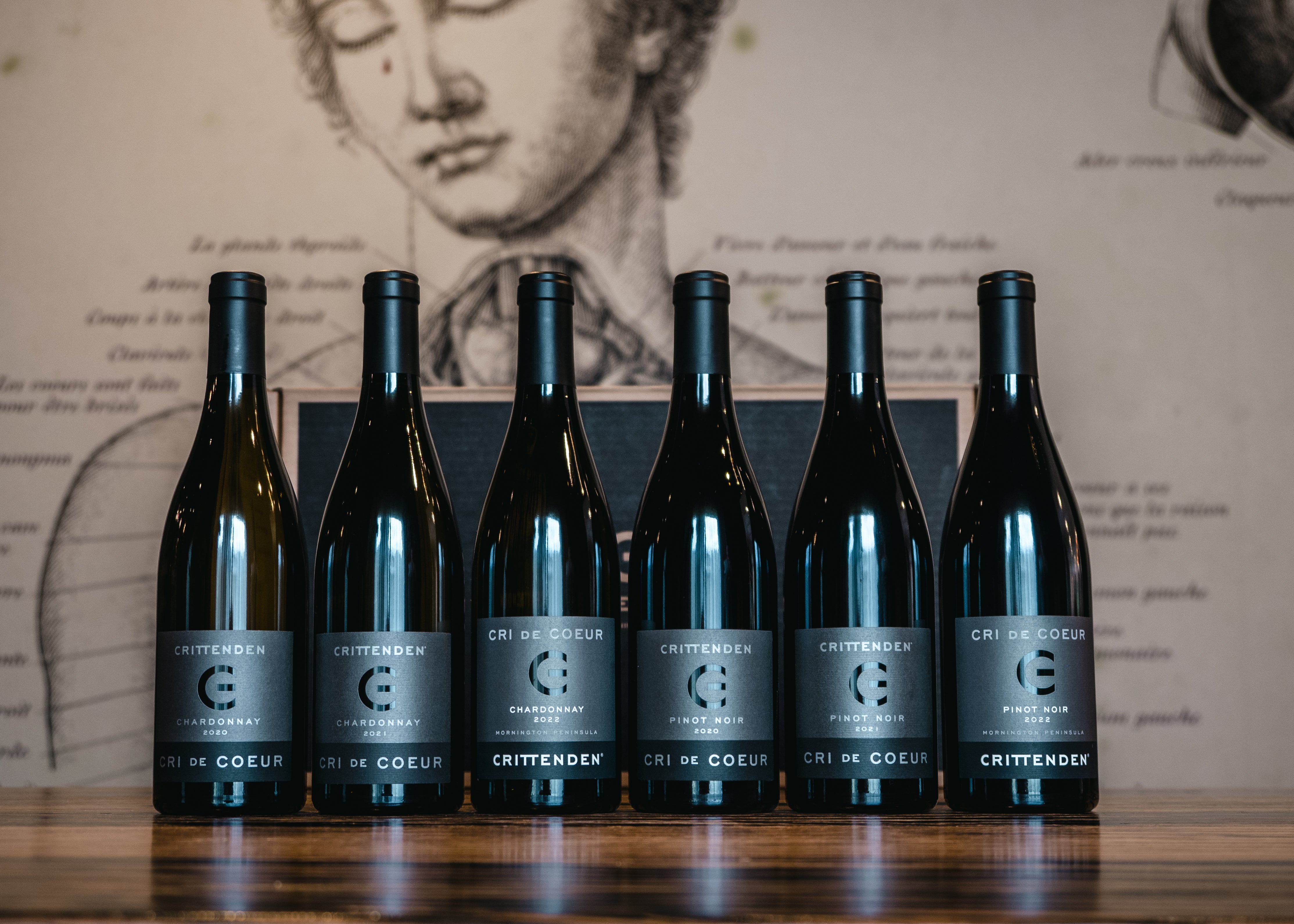 Six bottles of Cri de Coeur Chardonnay and Pinot Noir lined up on a timber bar