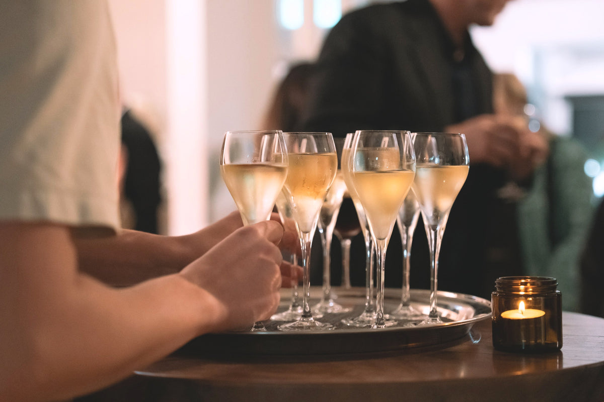 Glasses of sparkling wine on a tray at a Crittenden event, guests talking behind.