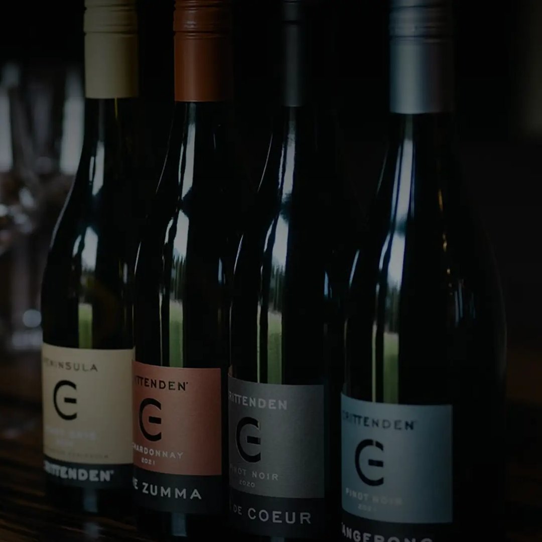 Four Crittenden wine bottles with colorful labels and silver, gold, and brown foil caps, lined up against a dark background.