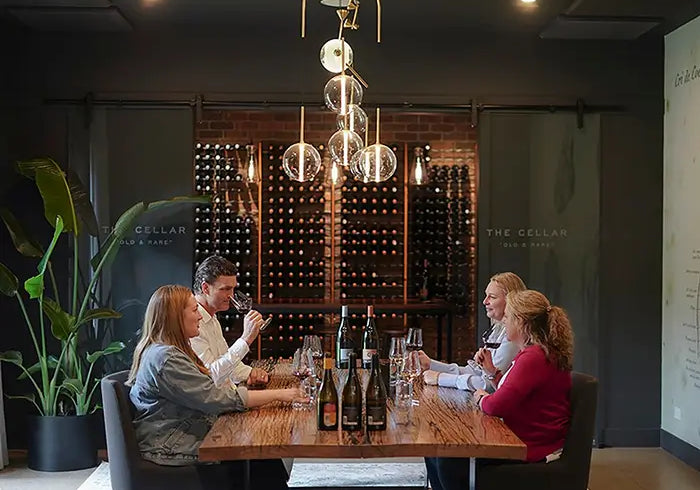Four guests tasting wine around a timber table in the private tasting room, with a wall of bottles behind them